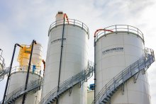 Three light colored manufacturing siloes as seen from the ground.